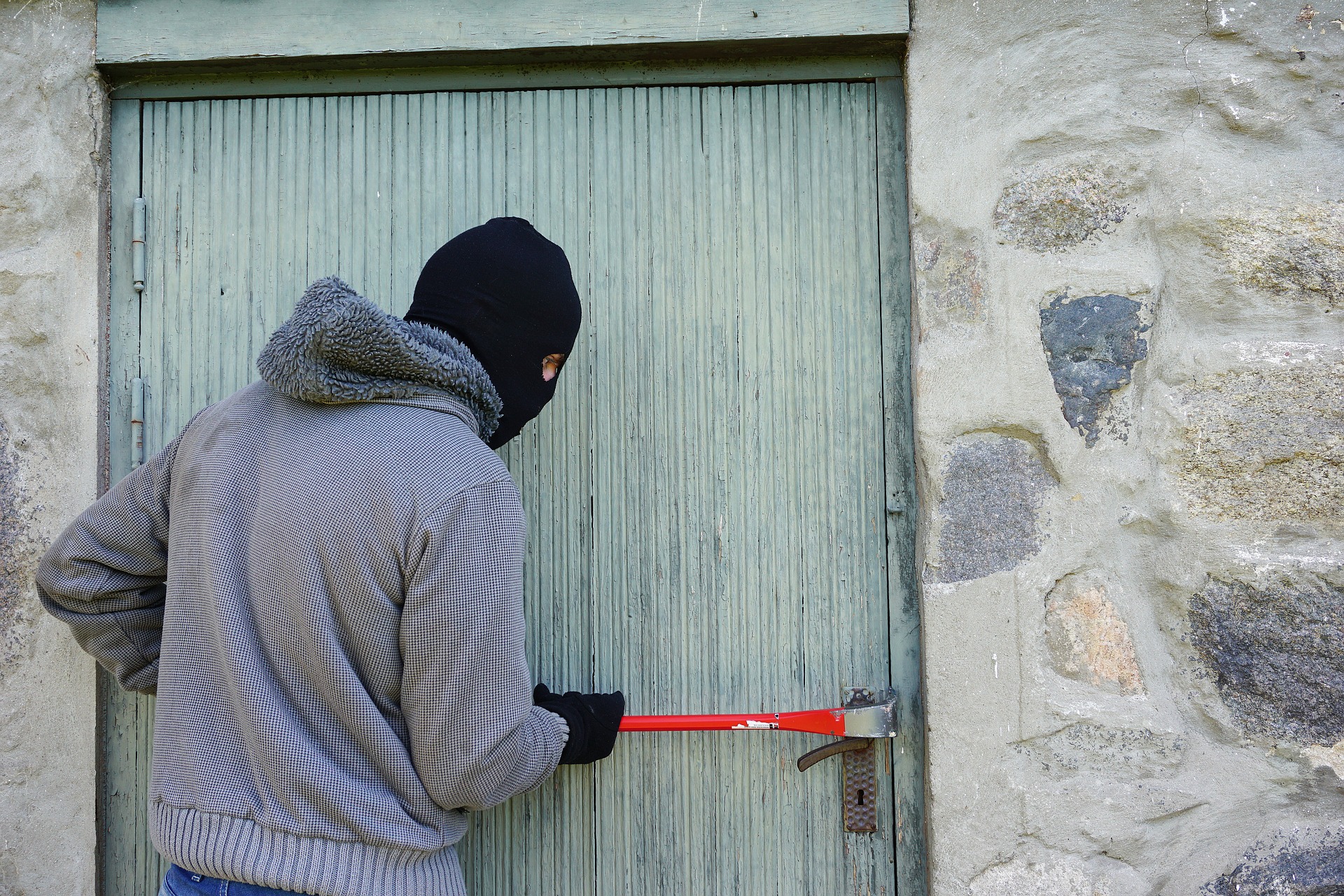 crime increase over the holidays - hooded person using crowbar to force open a door