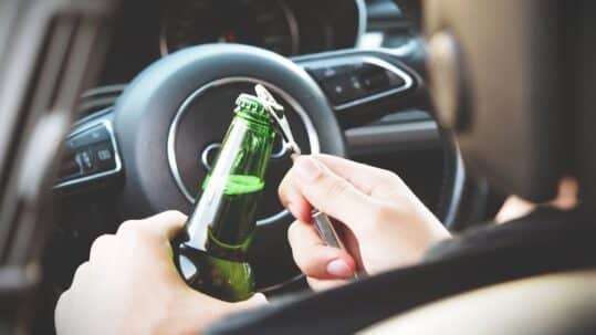 driver opening beer bottle in car